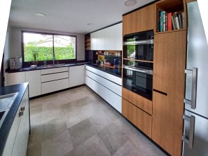 Cozinha com armários em tom escuro e bancada em pedra clara