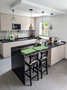 Cozinha moderna por medida em tom creme com bancada e península em granito preto e candeeiros suspensos.