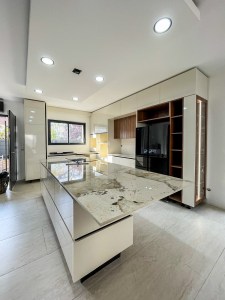 Cozinha de luxo fabricada por medida com ilha extensa em pedra natural, móveis lacados a branco brilhante e nichos em madeira com luz LED.