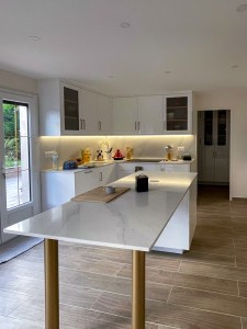 lha de cozinha por medida com balcão suspenso e pés cilíndricos dourados, integrada em cozinha aberta lacada a branco.